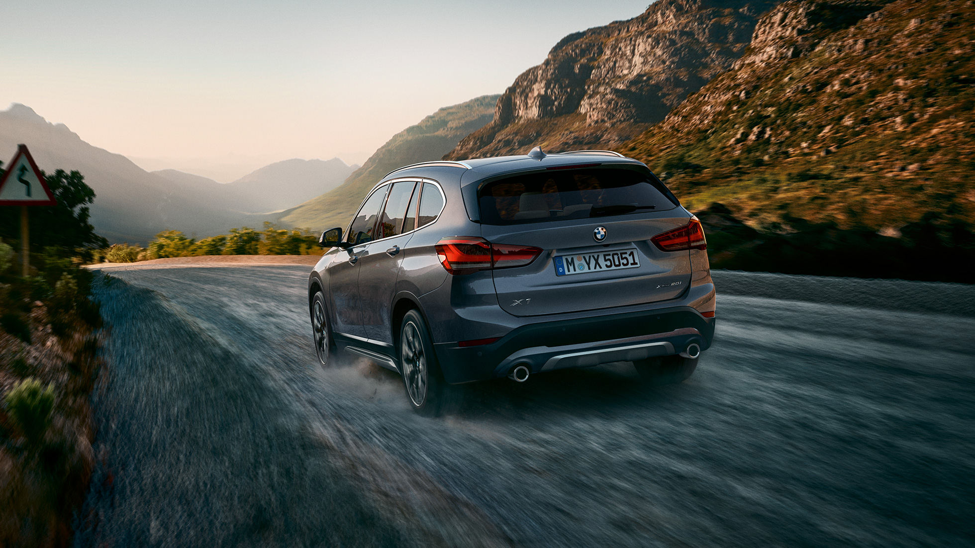 BMW X1, tričetrtinski pogled od zadaj. BMW X1, tričetrtinski pogled od zadaj med vožnjo pred gorsko pokrajino.