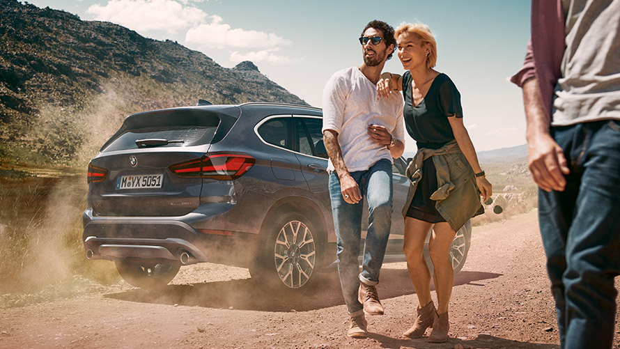 BMW X1, F48, LCI, barva Storm Bay, tričetrtinski pogled od zadaj BMW X1, F48, LCI, barva Storm Bay, tričetrtinski pogled od zadaj med mirovanjem v naravi z ljudmi v ospredju