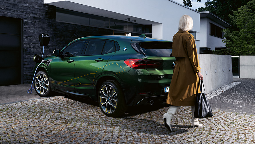 BMW X2, F39, kovinska barva Sanremo Green, tričetrtinski pogled od zadaj z manekenko BMW X2, F39, kovinska barva Sanremo Green, tričetrtinski pogled od zadaj z manekenko