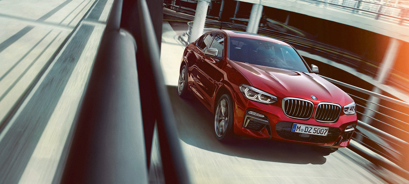 BMW X4 med vožnjo na parkirišču večnadstropne parkirne hiše BMW X4 G02 2018, Flamenco Red z briljantnim učinkom, tričetrtinski stranski pogled med vožnjo na parkirišču večnadstropne parkirne hiše