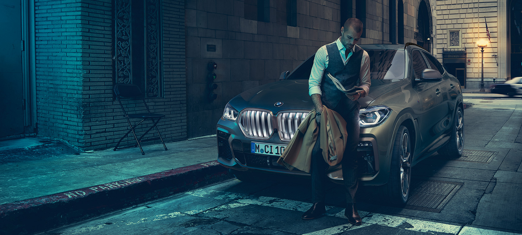 Moški se naslanja na BMW X6. Moški se naslanja na BMW X6 v stranskem pogledu v mestnem okolju.
