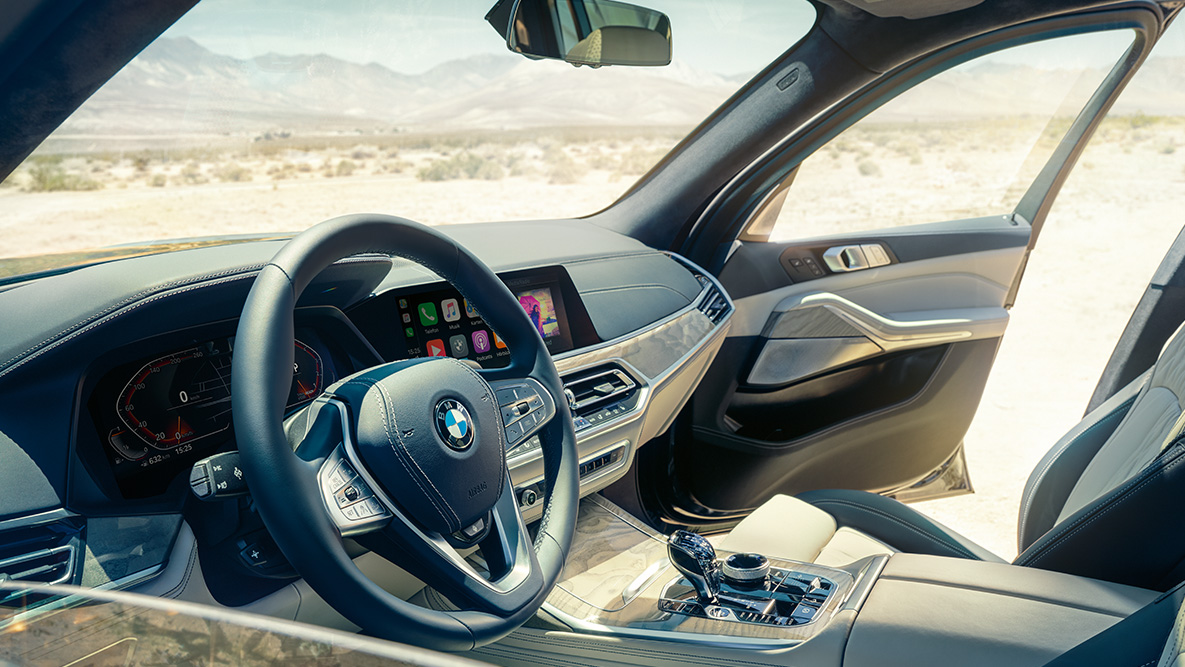 Notranjost vozila BMW X7 Notranjost vozila BMW X7: pogled od zunaj na prvo vrsto sedežev s pogledom na volan, instrumentno ploščo in usnjene sedeže