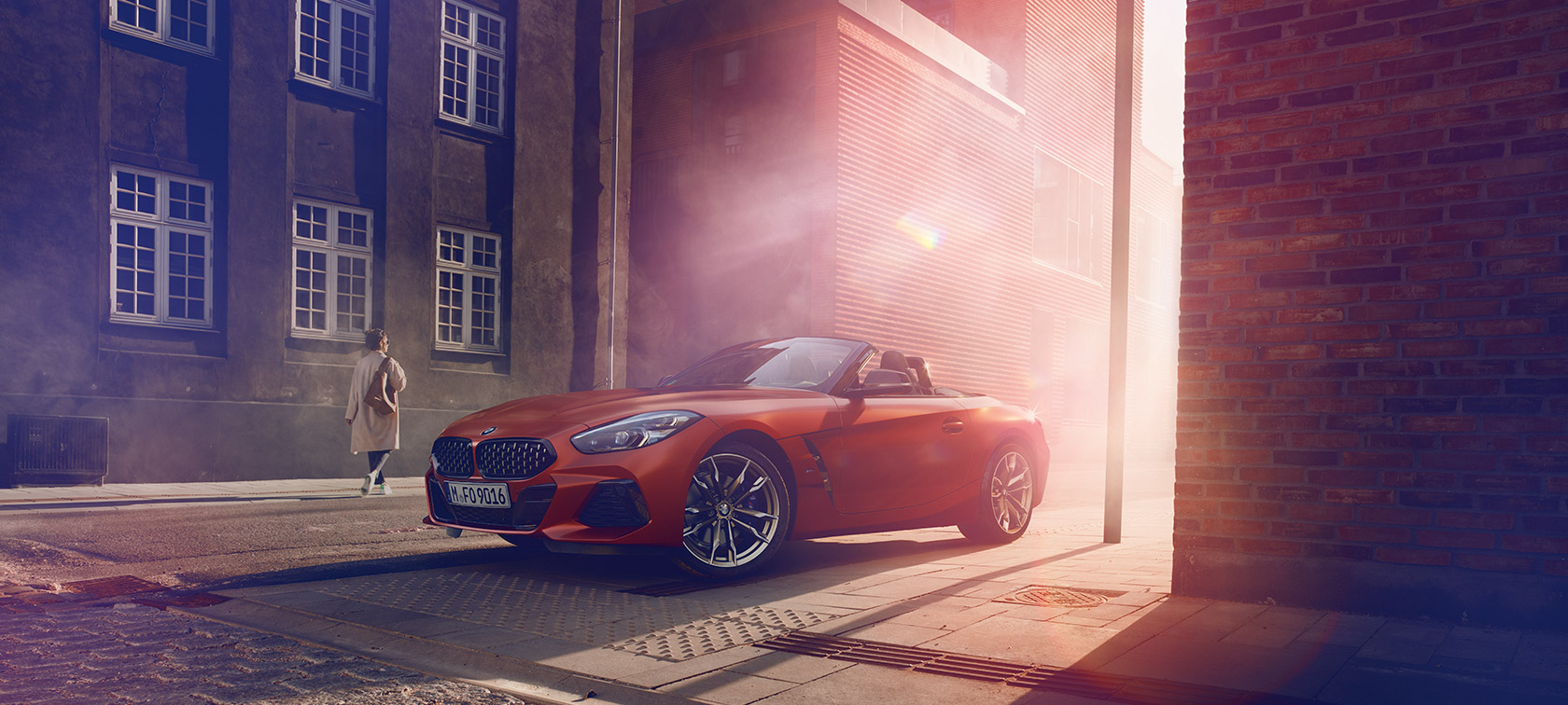 Rdeč BMW Z4 First Edition na ulici Rdeč BMW Z4 First Edition na delno zatemnjeni ulici pred vrsto hiš z žensko