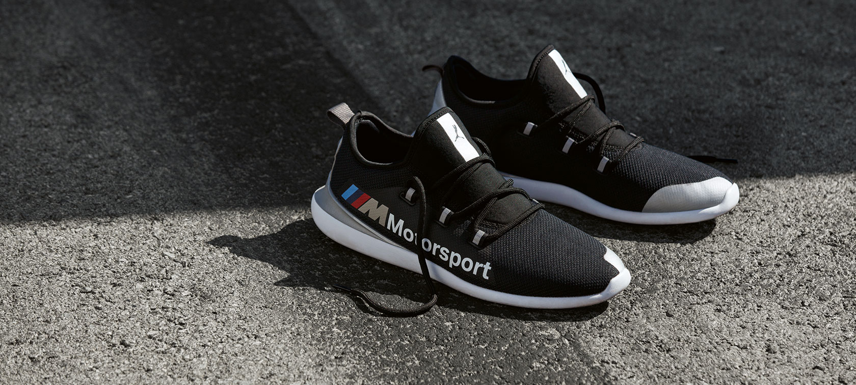 Čevlji BMW M Motorsport PUMA EVO CAT. Na sliki je par čevljev BMW M Motorsport PUMA EVO CAT iz kolekcije BMW M Motorsport na makadamski cesti.