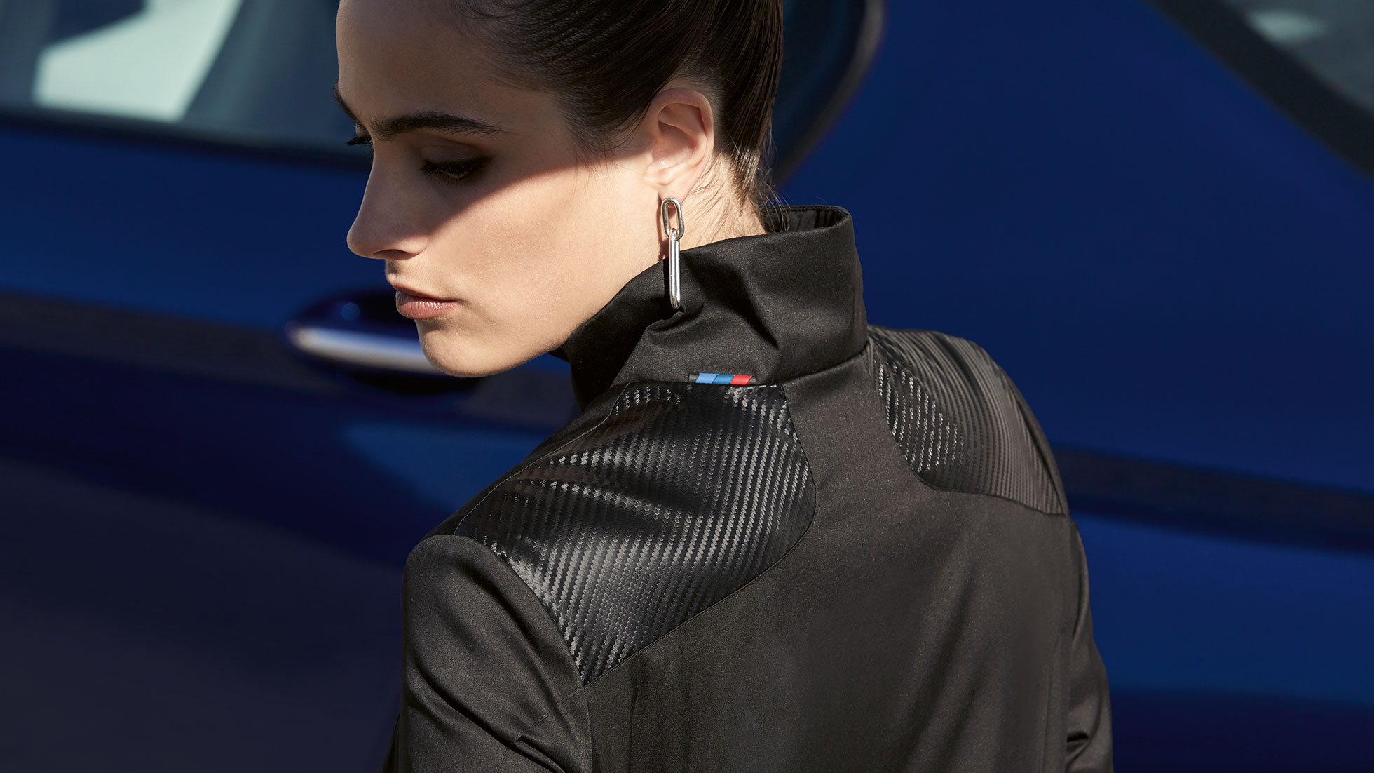 Ženska jakna BMW M. Na sliki je ženska, oblečena v žensko jakno iz kolekcije BMW M. Podrobnost mešanice materialov.