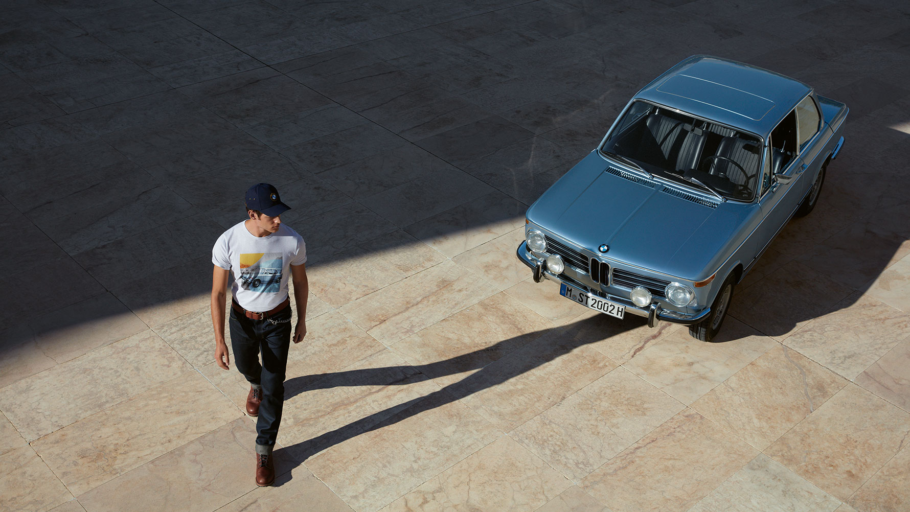 Moški na sliki je oblečen v moško majico s kratkimi rokavi iz kolekcije BMW Classic in občuduje klasičen model BMW. Moški na sliki je oblečen v moško majico s kratkimi rokavi iz kolekcije BMW Classic in občuduje klasičen model BMW.