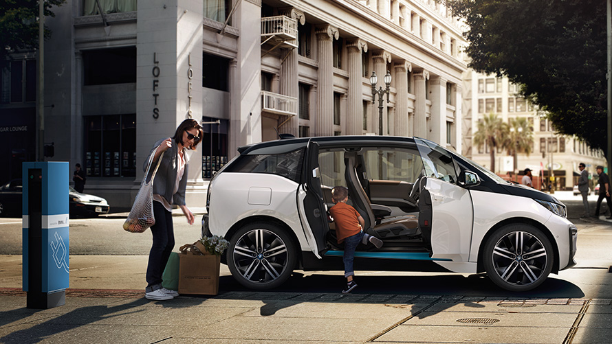 BMW i3 pred mestnim ozadjem Doseg BMW, BMW i3 pred mestnim ozadjem z žensko in otrokom