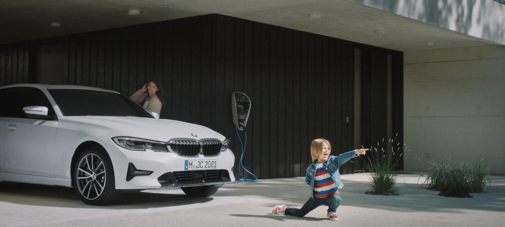Hibridno vozilo BMW pred polnilno postajo Priključni hibridi BMW, fant pred hibridnim vozilom BMW pri polnilni postaji