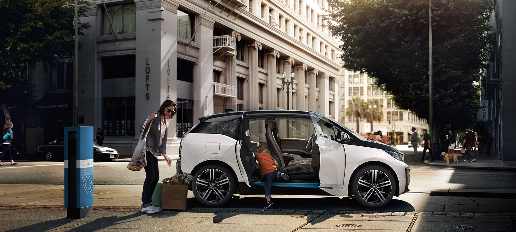 BMW i3 pred mestnim ozadjem Doseg BMW, BMW i3 pred mestnim ozadjem z žensko in otrokom