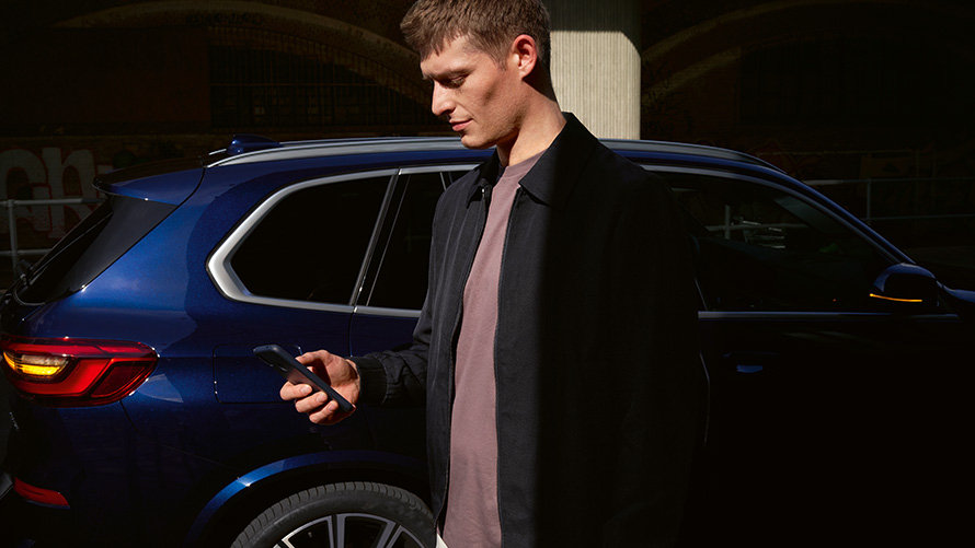 BMW Digital Key – namestite do pet uporabnikov BMW Digital Key, namestite do pet uporabnikov, moški s pametnim telefonom stoji pred BMW X5