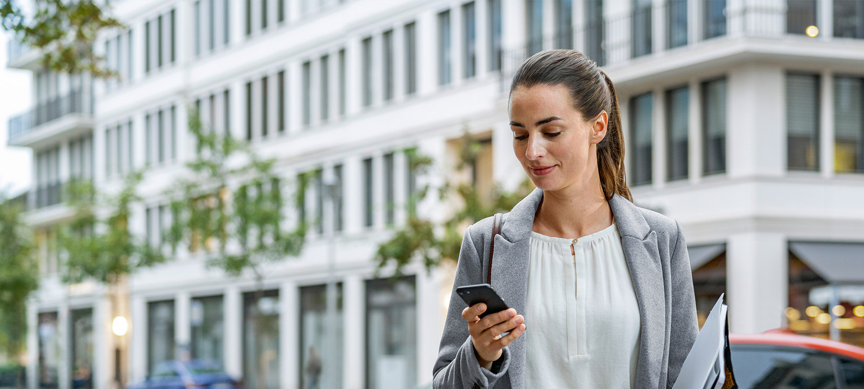 Ženska stoji pred stavbo in gleda svoj pametni telefon Remote Software Upgrade, ženska stoji pred stavbo in gleda svoj pametni telefon