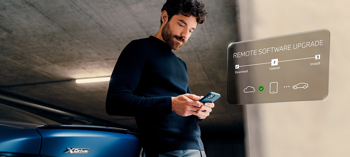 Moški se naslanja na zadek BMW in gleda svoj pametni telefon Remote Software Upgrade, moški se naslanja na zadek BMW in gleda svoj pametni telefon