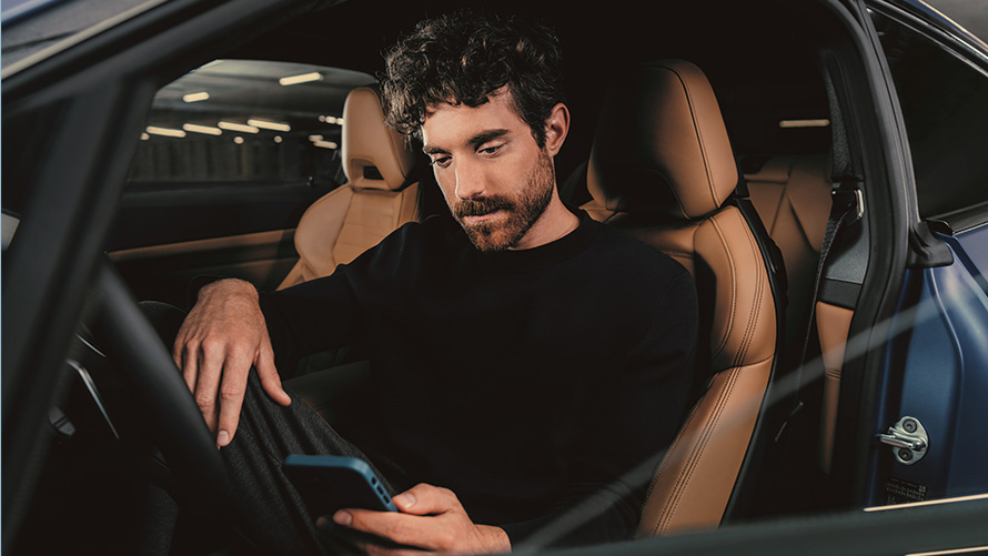 Moški sedi v BMW Moški sedi v BMW in gleda svoj pametni telefon
