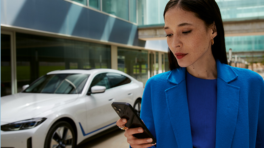 Ženska stoji pred BMW Ženska stoji pred BMW in gleda v svoj pametni telefon
