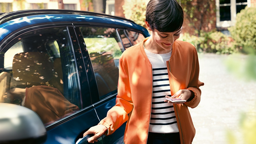 BMW Teleservices Ženska s pametnim telefonom stoji pred vrati svojega BMW