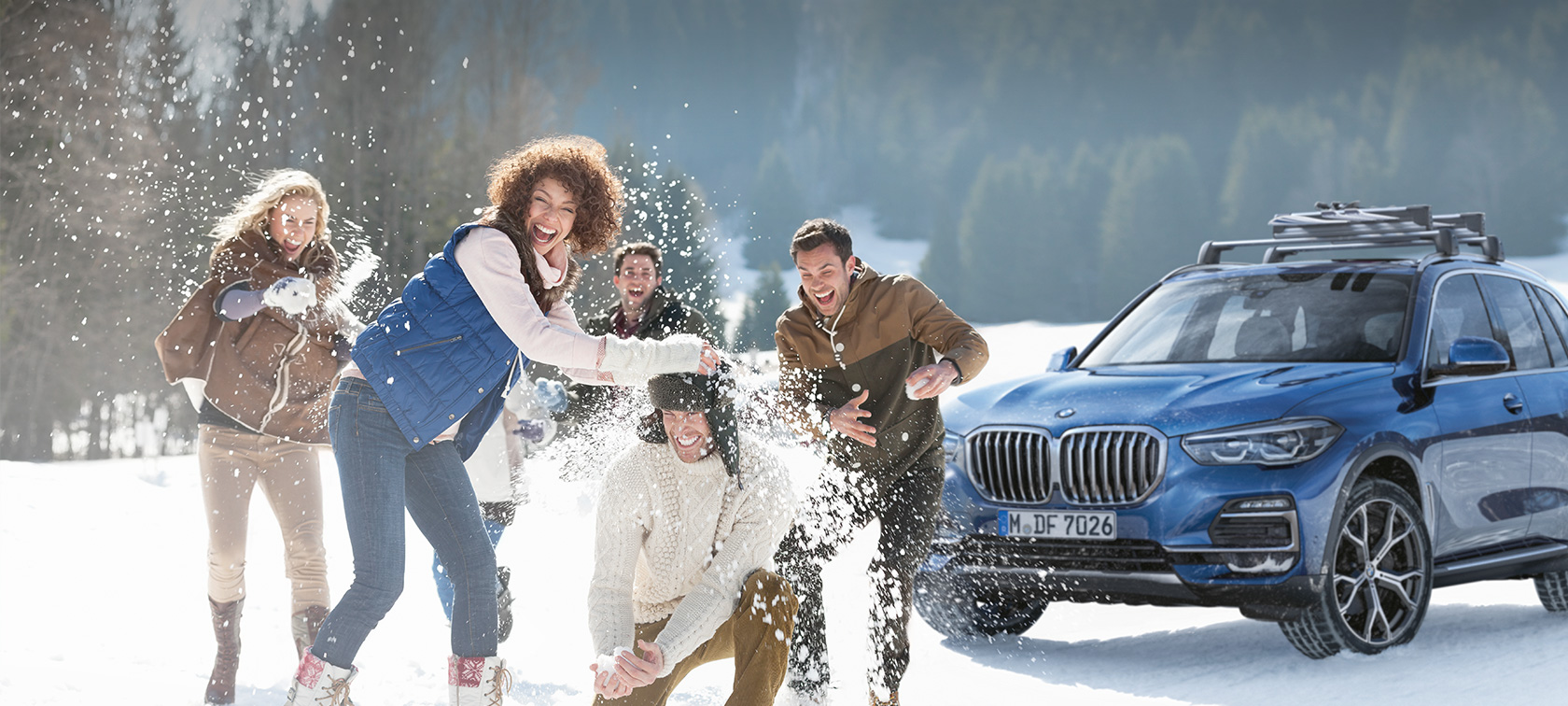 Originalna dodatna oprema BMW in BMW Service za jesen in zimo Moški in ženska stojita pred BMW v gozdu