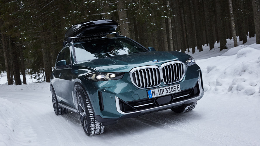 Zimski kompleti koles BMW na BMW X5 (G05 LCI) na zasneženi cesti v gozdu Zimski kompleti koles BMW pri BMW X5 (G05 LCI) na zasneženi cesti v gozdu