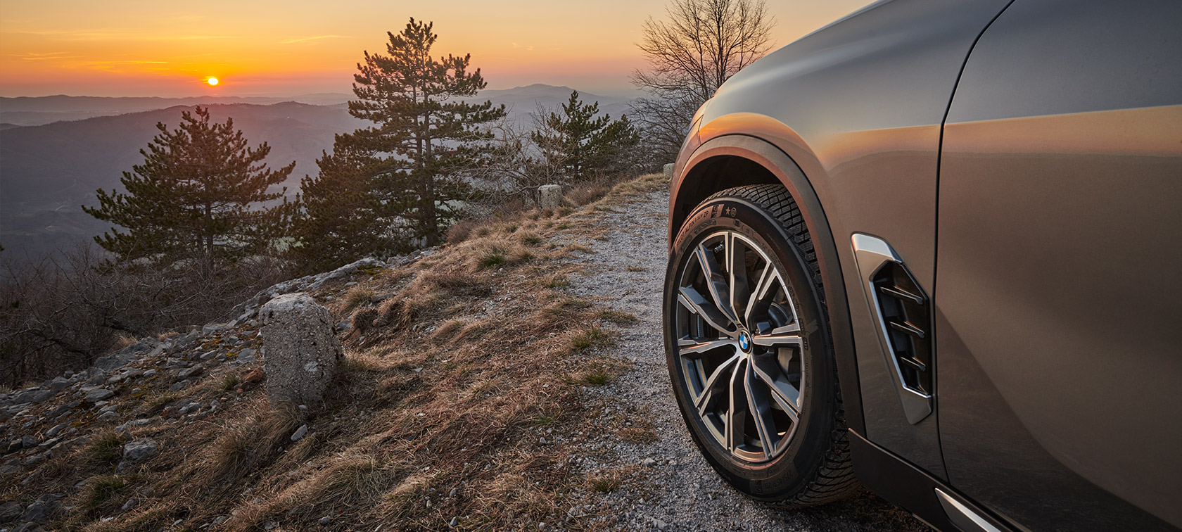 Originalna platišča BMW na BMW X5 (G05 LCI) na makadamski cesti na pobočju gore, obrnjen proti sončnemu zahodu Originalna platišča BMW na BMW X5 (G05 LCI)