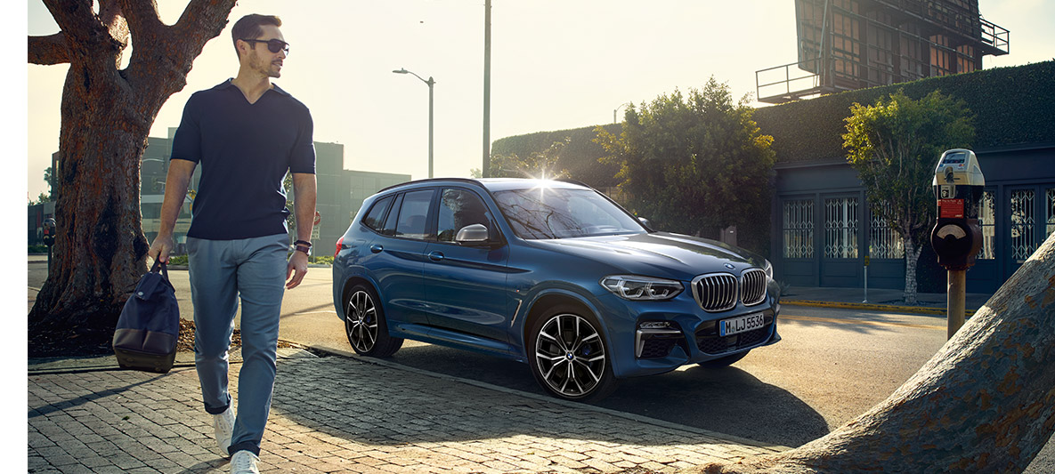 Moški s sončnimi očali pred modrim vozilom BMW Moški s sončnimi očali pred modrim vozilom BMW