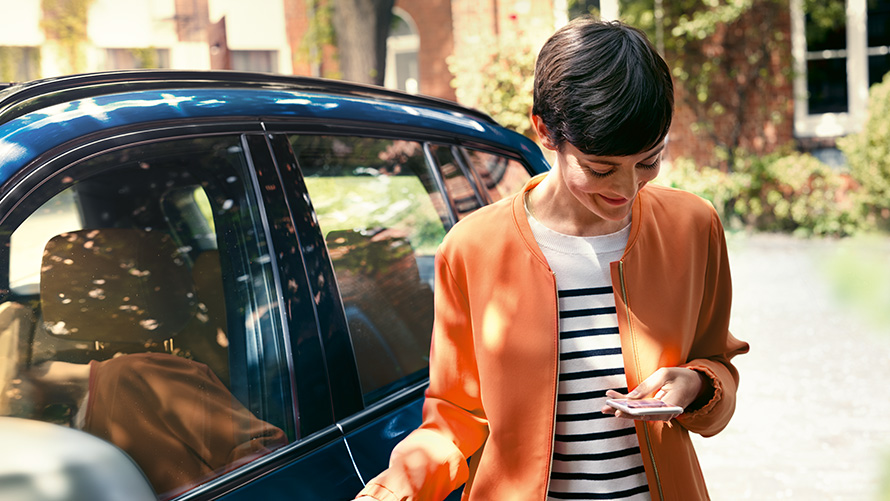 Poletne ponudbe BMW, BMW Teleservices Poletne ponudbe BMW, BMW Teleservices, ženska stoj pred BMW in uporablja pametni telefon