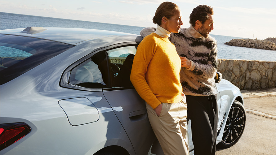 Trajanje in pogodbena obdobja BMW Service Inclusive za nova vozila BMW Service Inclusive, moški in ženska se naslanjata na BMW i4 ob obali¤