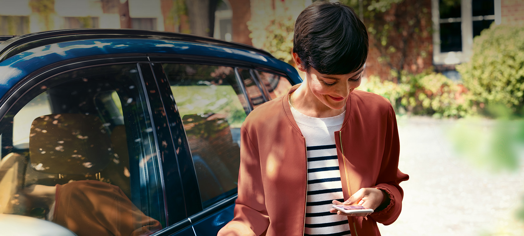 BMW Teleservices, ženska gleda svoj pametni telefon BMW Teleservices, ženska pred BMW-jem gleda svoj pametni telefon
