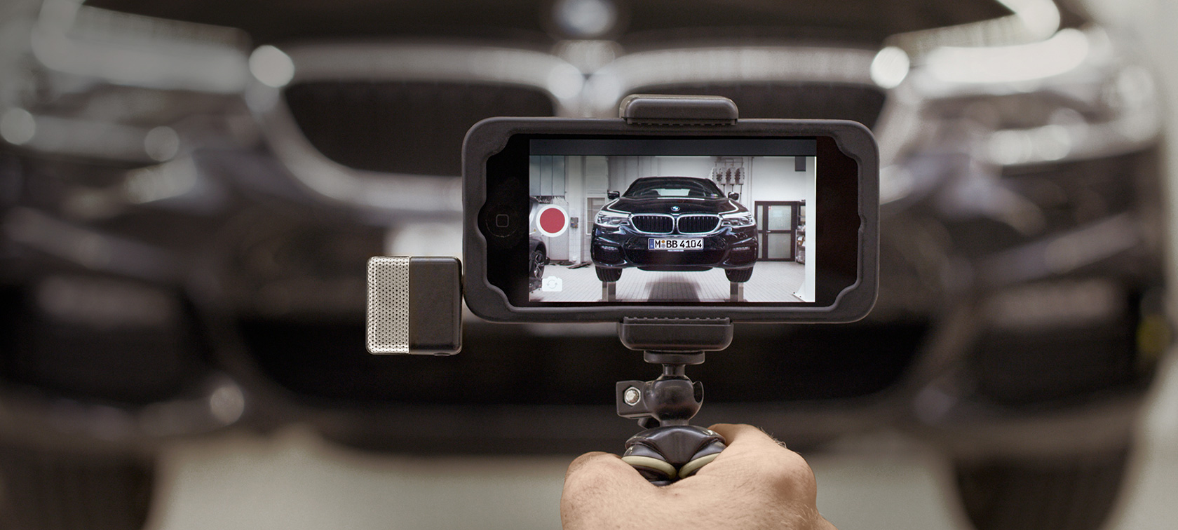 BMW Service Video on smartphone BMW Service Video runs on smartphone in front of a BMW