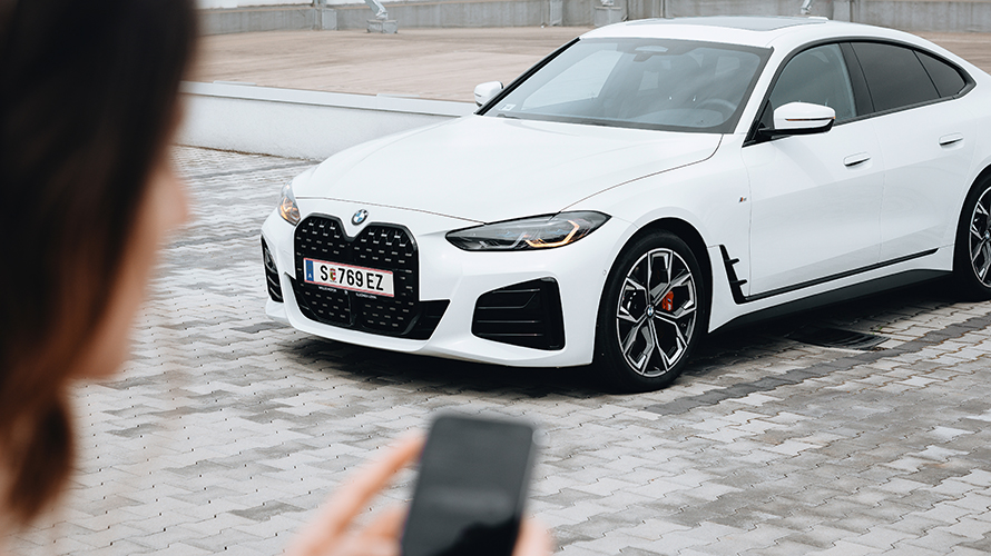 Ženska uporablja pametni telefon. Fokus je na BMW i4. Ženska uporablja pametni telefon. Fokus je na BMW i4.