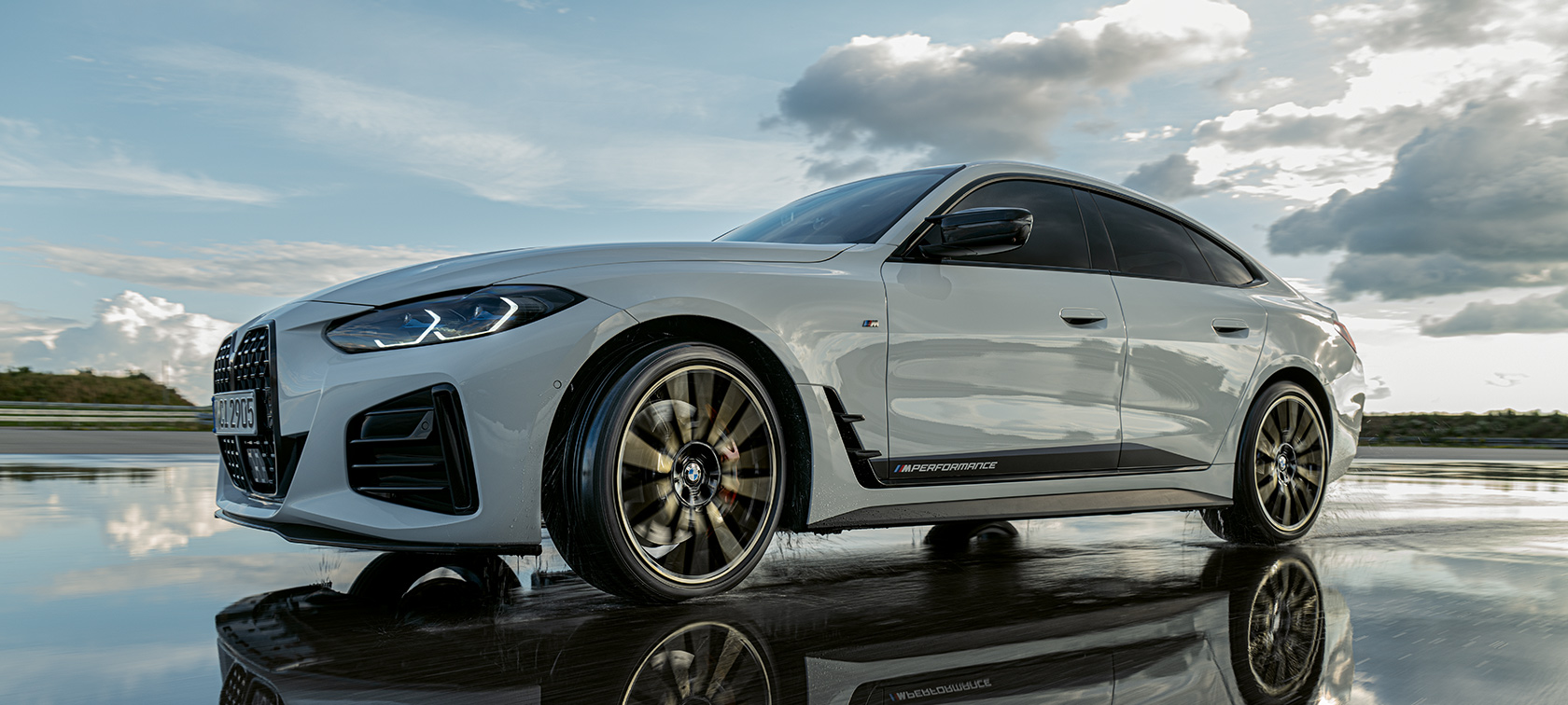 Moški s psom, prislonjen ob BMW BMW M440i na odsevnih in mokrih tleh.