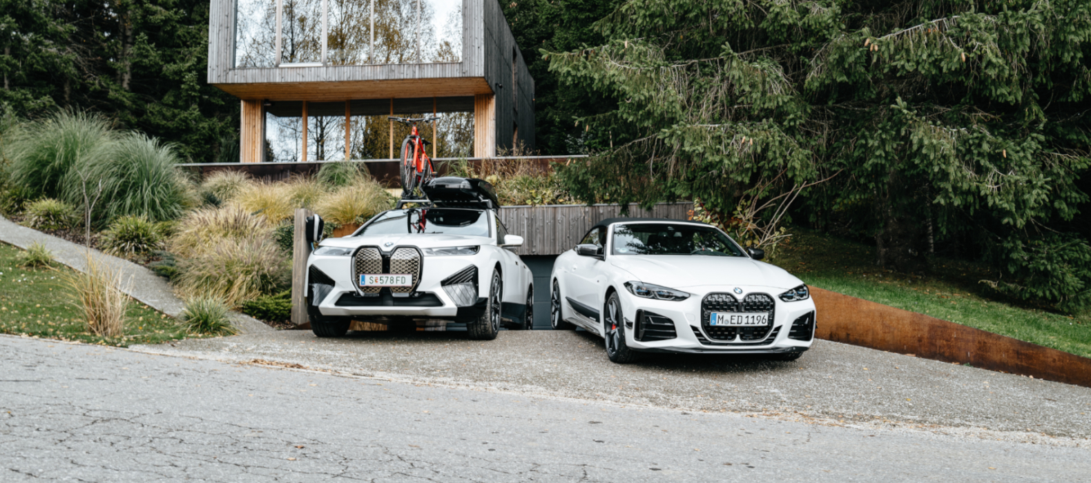 BMW IX z dodatno opremo in BMW M440i stojita pred moderno hišo. BMW IX z dodatno opremo in BMW M440i stojita pred moderno hišo.
